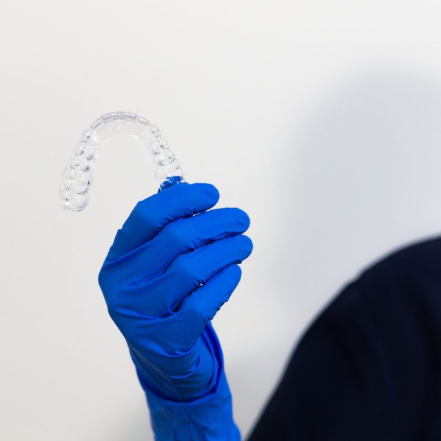 A closeup shot of a dentist with gloves holding a transparent dental splint