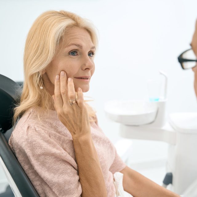 Charming Caucasian female is sitting in dental chair while having discuss with doctor about the gum pain in dentistry center